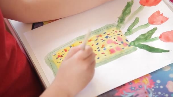 Het meisje trekt op papier bloemen in een vaas, een penseel met aquarelverf. — Stockvideo