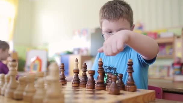 Ein Junge mit Brille spielt Schach. Er sitzt am Tisch und spielt und lächelt emotional. er will Schachmatt setzen und gewinnen. — Stockvideo