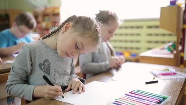 Τα κορίτσια δίδυμων αδελφών ζωγραφίζαν με στυλό σε χαρτί σε ένα τραπέζι σε μια τάξη. Τα νήπια κάνουν καλλιτεχνική εκπαίδευση στο σχολείο — Αρχείο Βίντεο