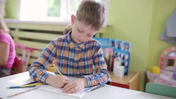 O menino de 6 anos em uma classe em uma mesa de escola executa uma tarefa em um caderno. Preparação Escolar Pré-escolar — Vídeo de Stock