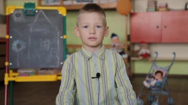 Ekose gömlekli bir çocuk kameranın önündeki sandalyeye oturmuş kıyafetlerinde mikrofonla soruları cevaplıyor..