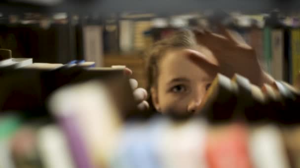 Dziewczyna wybiera książki na półce w bibliotece. Sporo książek do nauki.. — Wideo stockowe