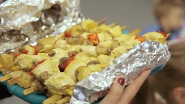 Folyoda pişirilmiş tavuk şişleri. Kadın bitmiş tabağı çelikten folyoya taşıyor.