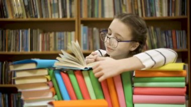 Gözlüklü kız kütüphanede kitap karıştırıyor.