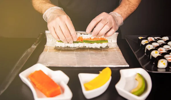 Cook hands making Japanese sushi roll. Japanese chef at work preparing delicious sushi roll with eel and avocado