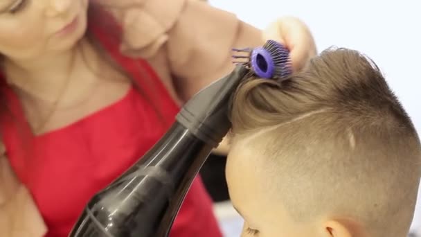 Dziewczyna fryzjer umieszcza włosy w suszarce do włosów, a grzebień robi fryzurę dla chłopca. — Wideo stockowe
