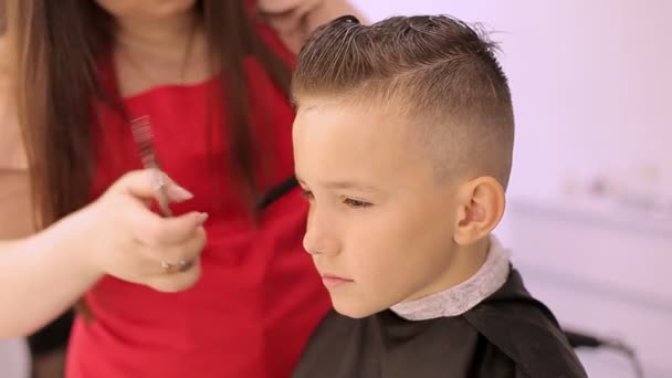 Дівчина перукар ріже волосся ножицями і гребінець робить перукарню для хлопчика . — стокове відео