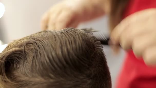 Het meisje de kapper knipt haar met een schaar en een kam doet een haarjurk aan de jongen. — Stockvideo