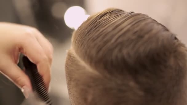 Het meisje de kapper knipt haar met een schaar en een kam doet een haarjurk aan de jongen. — Stockvideo