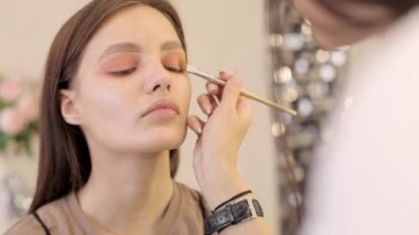 Makyaj sanatçısı göz farı sürüyor. Güzel bir kadın yüzü. Makyöz, genç bir güzellik mankeni kızın el makyajını yapıyor. Güzellik stüdyosunda makyaj malzemesi.