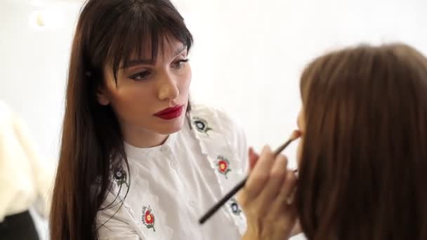 Make-up kunstenaar brengt oogschaduw. Prachtig vrouwelijk gezicht. Make-up kunstenaar hand schilderen make-up van jonge schoonheid model meisje. Make-up in het proces beauty studio — Stockvideo