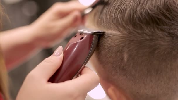 Flickan frisören klipper håret med en maskin och kamma gör frisyren till pojken Frisör som handlar med frisyr frisyr pojke Plats för arbete frisör Detta barn har en ny frisyr — Stockvideo
