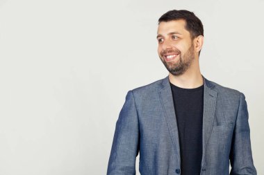 Yakından ceketli sakallı yakışıklı bir adam profilde duruyor, yan tarafa bakıyor, fotoğraf için poz veriyor. Yüzünde bir gülümseme, doğal bir ifade olan bir adam diğer tarafa bakıyor..