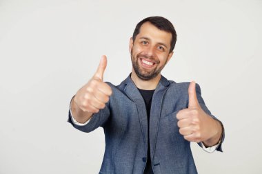 Ceketli, sakallı, olumlu el hareketi yapan, gülümseyen ve başarı için sevinen genç bir işadamı. Kazananın jesti Gri arka planda bir adamın portresi