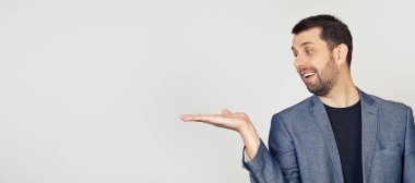 Beyaz tişörtlü, sakallı, gülümseyen, neşeli bir şekilde avuç içini gösteren ve eline bakan genç bir adam. İzole edilmiş sarı arkaplanda durur