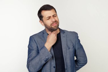 Sakallı genç işadamı boynuna dokunuyor. Grip, yumru ve enfeksiyon yüzünden boğazı ağrıyor. Gri arka planda bir adamın portresi.
