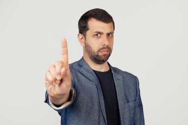 Ceketli, sakallı genç bir işadamı parmağını kaldırıyor ve hareketsiz sinirli bir ifade takınıyor. Gri arka planda bir adamın portresi.