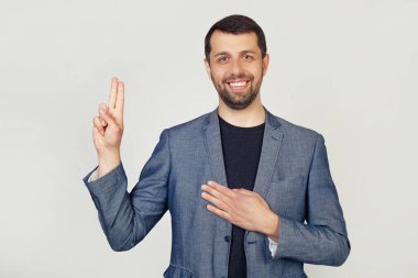 Ceketli, sakallı, gülümseyen, küfreden, elini göğsüne koyup, sadakat yemini eden genç bir işadamı. Gri arka planda bir adamın portresi.