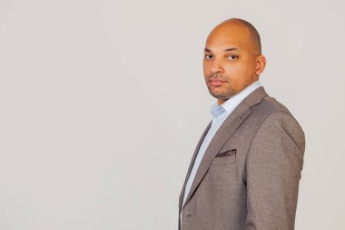 Ceketli yakışıklı, Afro-Amerikan bir iş adamı yüzünde ciddi bir ifadeyle kameraya bakıyor. Gri arkaplanda bir fotoğraf için poz vermek