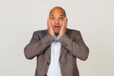 Şok olmuş genç Afro-Amerikalı iş adamı şaşkınlık ve şaşkınlık içinde yüzüne dokunuyor ve dudaklarını katlıyor, sersemlemiş bir şekilde kameraya bakıyor ve etkileniyor..