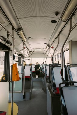 Güneş gözlüklü şık bir kadının parlak, boş bir otobüsün arkasında tek başına oturması geniş açılı bir bakış açısı. Şehir içi ulaşımı, bağımsızlığı ve sessiz ulaşım anlarını tasvir etmek için birebirdir..