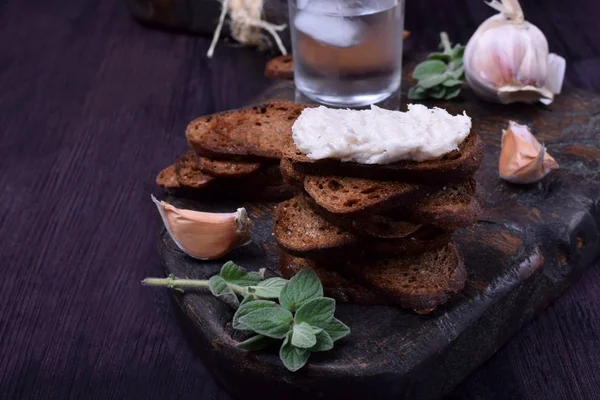 Rye bread toasts, lard paste and a misted glass of vodka on a black board. Ukrainian cuisine appetizer — Stock Image Rye Bread Toasts Lard Paste Misted Glass Vodka Black Board Stock Photo