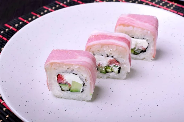 Japanese rolls with bacon, cheese, rice, salmon and cucumber on a white plate