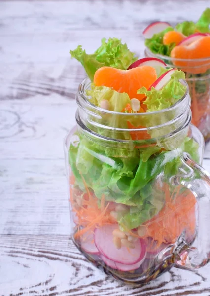 Layered salad in a jar with mandarins, radish, lettuce leaves, carrot and dressing