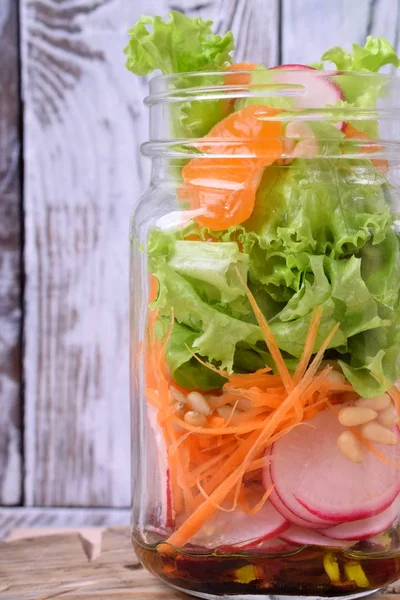 Layered salad in a jar with mandarins, radish, lettuce leaves, carrot and dressing