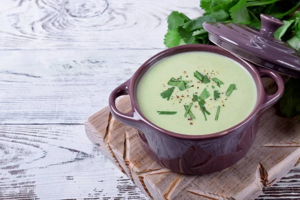Green cream soup in a ceramic pan against the white wooden background