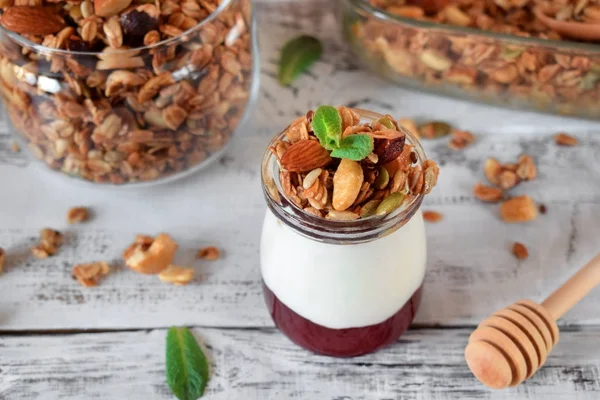 Layered breakfast with granola, yogurt and jam in a glass jar on the white table