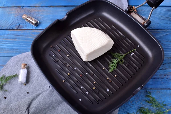 Quarter of adyghe cheese on the griddle pan is prepared for grilling