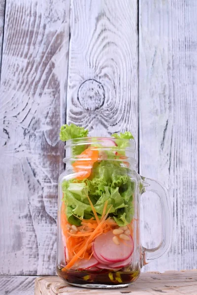 Layered salad in a jar with mandarins, radish, lettuce leaves, carrot and dressing