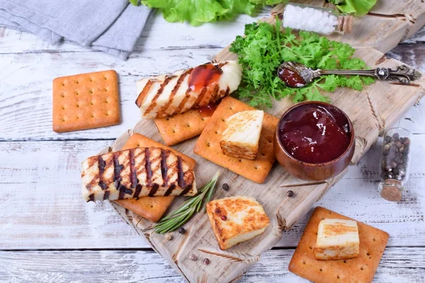 Grilled adyghe cheese, crackers, red jam, spices and cress salad on the wooden board against the white background
