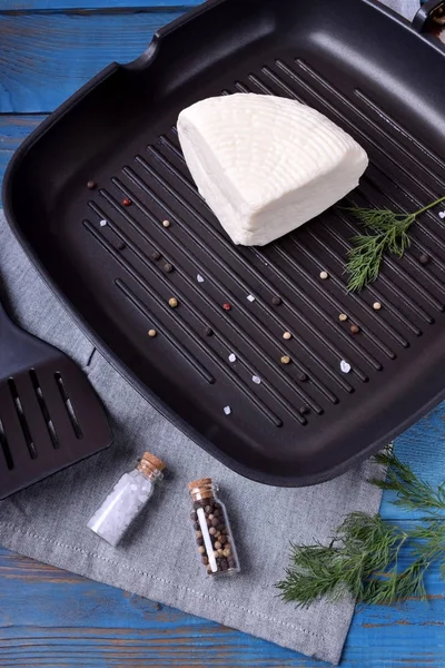 Quarter of adyghe cheese on the griddle pan is prepared for grilling