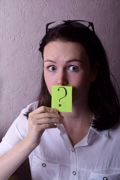 Young woman is holding a green sticker with a question mark against her face