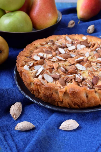 Pie with pears, apples and almonds on a black ceramic plate surrounded by the ingredients