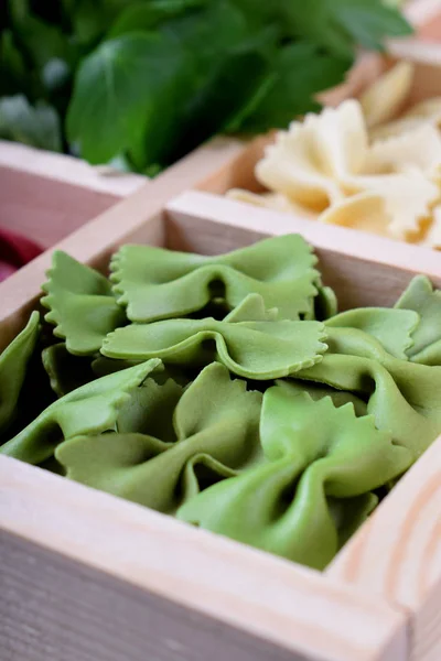 Green pasta farfalle in a wooden box. Multicolored pasta in the background
