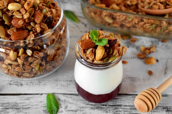 Layered breakfast with granola, yogurt and jam in a glass jar on the white table