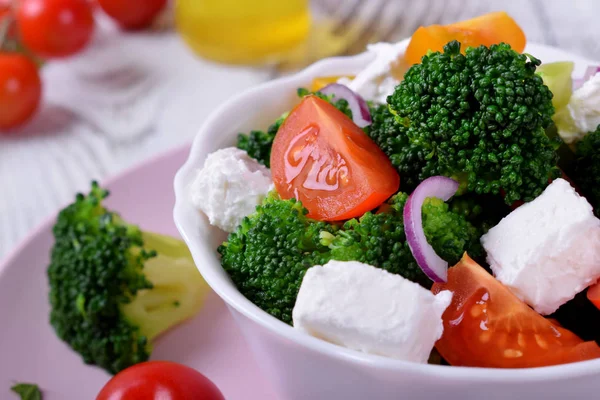 Light salad with broccoli, cherry tomatoes and feta cheese in a white ceramic bowl