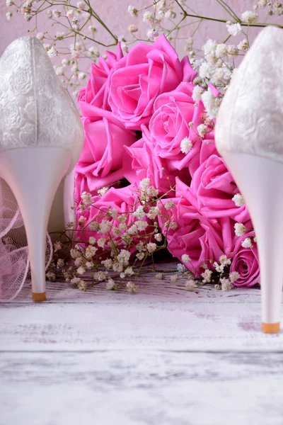 White heels and bouquet of pink roses on white table. Wedding composition