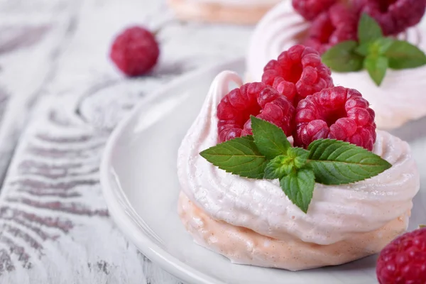 Mini Pavlova cake topped with raspberries and mint on white wooden table
