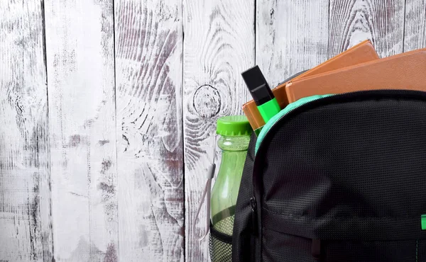 Black backpack with books, marker and bottle against white wooden wall