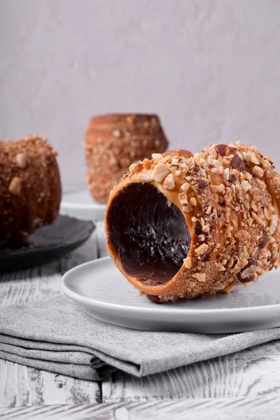 Trdelnik covered in nuts and sugar with chocolate inside against white wooden background. Czech street food