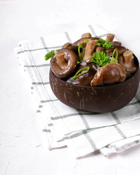 Pickled milk mushrooms with onion and spices topped with parsley in wooden bowl on the white table. Russian cuisine appetizer