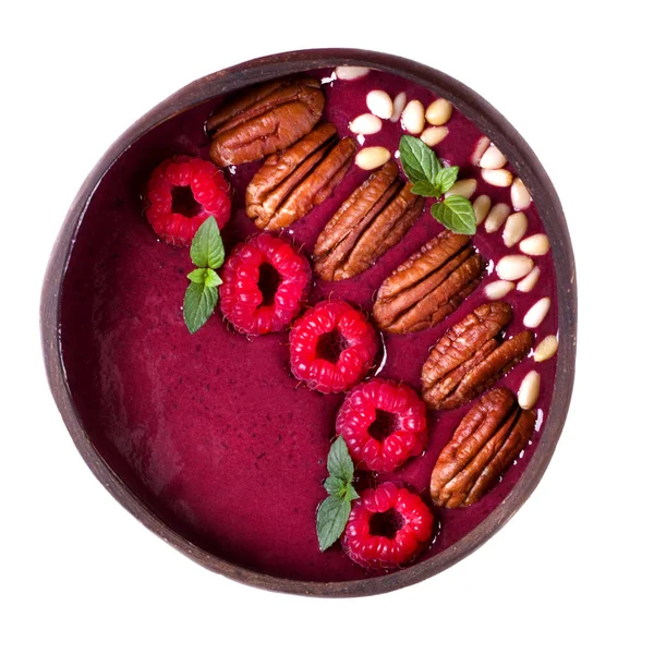 Smoothie bowl with raspberry, pecan, pine nuts and mint in a wooden bowl isolated on white
