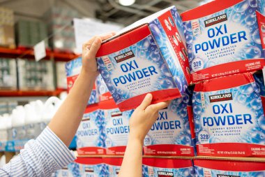 Bir müşterinin eli Costco rafından bir kutu Kirkland imzalı Oxi pudrası alıyor.