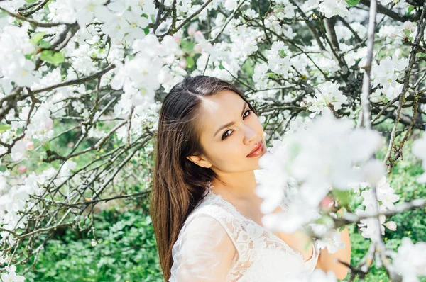Kameraya gülümseyen genç kız çiçeği elma bahçesinde beyaz elbiseli portresi