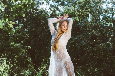 Genç güzel kız beyaz dantel elbise elma bahçesinde poz, kameraya bakıyor