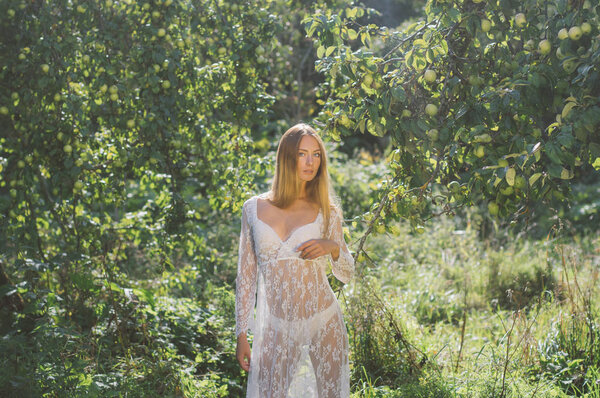 Young beautiful girl in white lace dress in apple garden